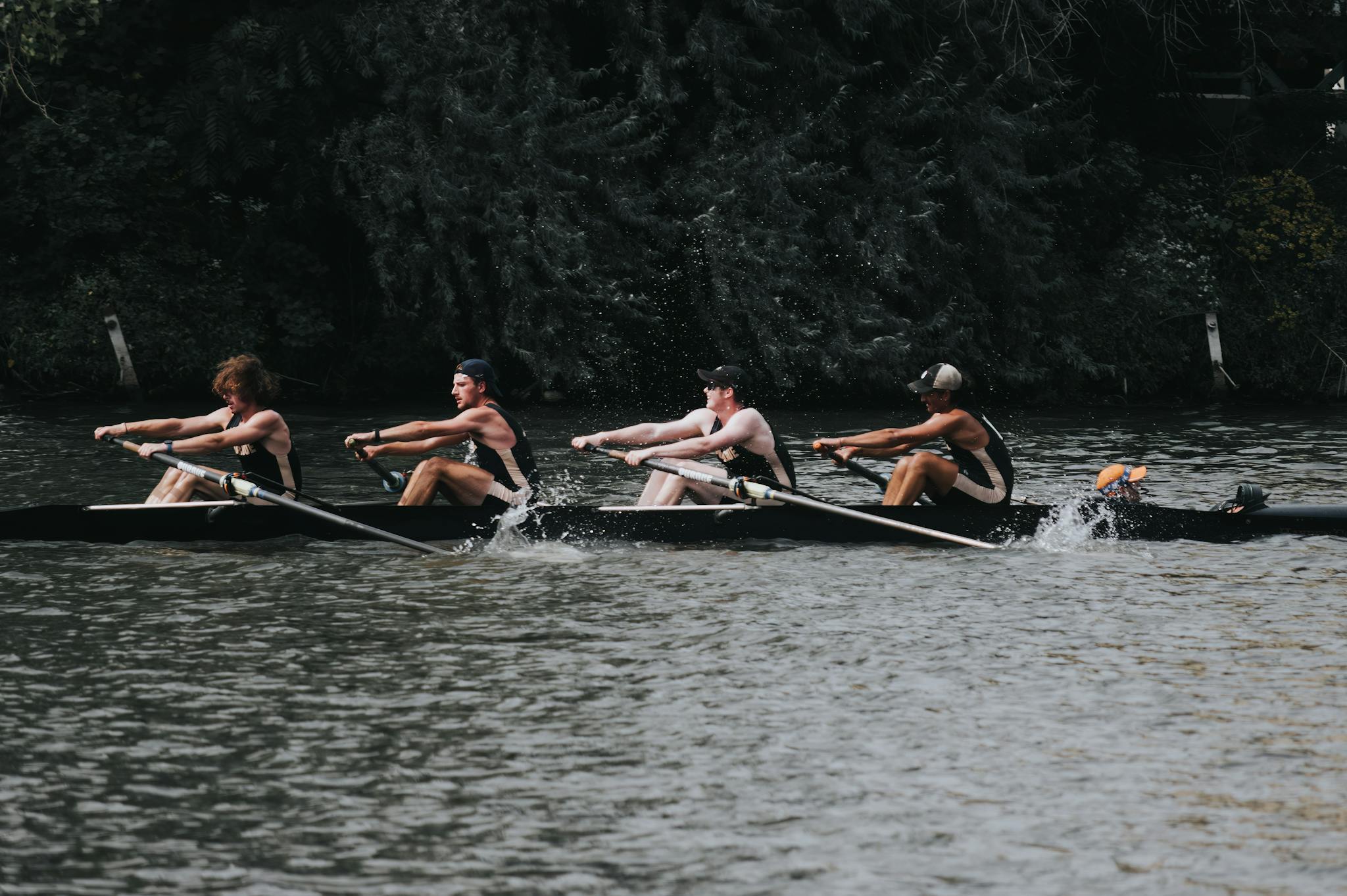 Four men engage in rowing practice on a river in Milwaukee during the day.