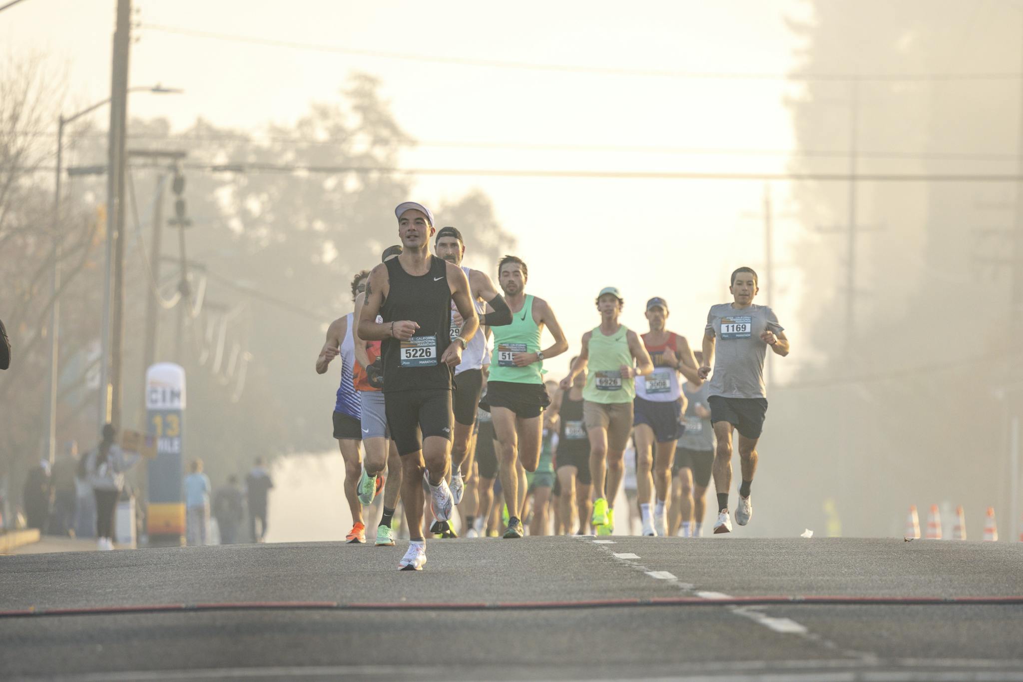 Group of runners in a marathon race on a foggy morning street with trees in the background.